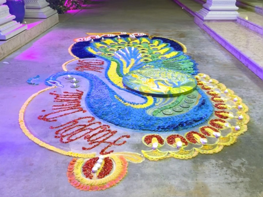 Artist seated beside the completed Rangoli at Radha Madhav Dham